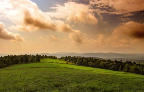 A scenic landscape featuring rolling green hills under a cloudy sky with distant mountains.