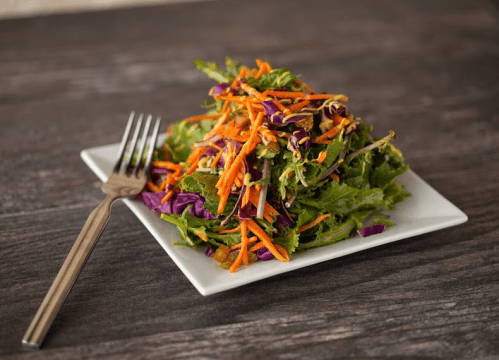 A fresh salad with mixed greens, purple cabbage, and shredded carrots on a square white plate, accompanied by a fork.