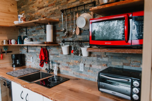 A cozy kitchen with wooden shelves, a red microwave, and a countertop with cooking utensils and appliances.