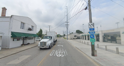 A street scene featuring a truck, power lines, and nearby buildings with a bike lane and signage.