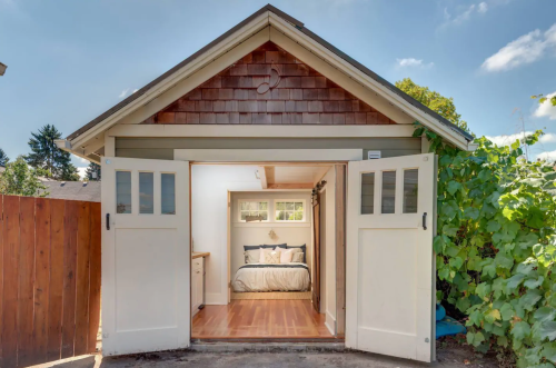 Cozy bedroom in a garage with double doors open, surrounded by greenery and a clear blue sky.