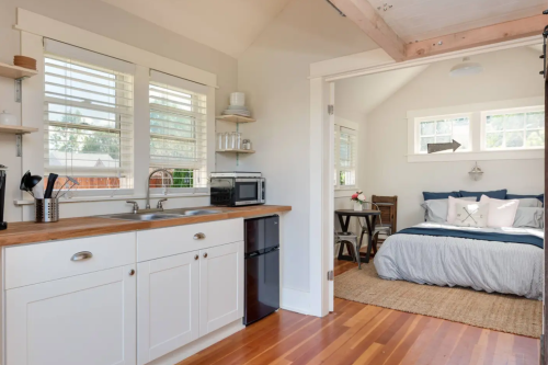 Cozy studio with a kitchenette, dining area, and a bed, featuring natural light and wooden accents.