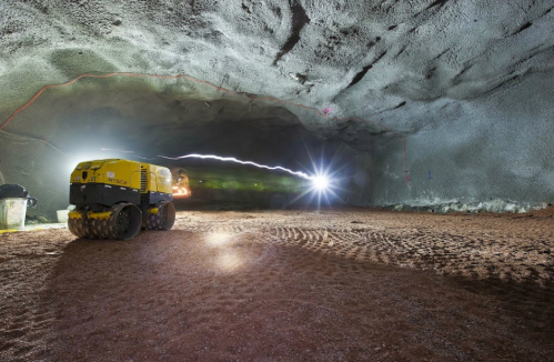 A large, dimly lit cave with a yellow construction vehicle and bright lights illuminating the rocky walls.