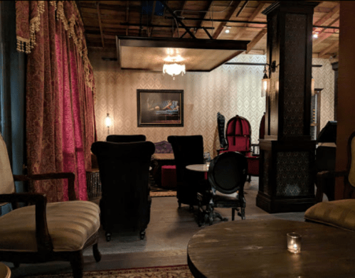Cozy, dimly lit lounge with ornate decor, plush seating, and rich curtains, creating an inviting atmosphere.