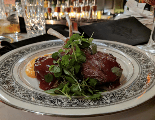 A plated dish featuring lamb chops topped with fresh greens and a berry sauce, served on an ornate plate.