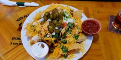 A plate of nachos topped with cheese, jalapeños, lettuce, tomatoes, onions, and served with salsa and sour cream.
