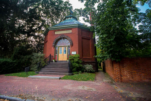 A brick building with a green dome, surrounded by trees and a pathway, featuring a set of stairs and a welcoming entrance.