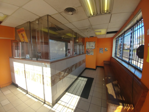 Interior of a fast-food restaurant with an orange theme, counter, and seating area, featuring large windows and a clean layout.
