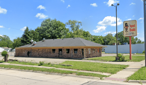 A brick building with a sign for "Spud Heads" and a grassy area, under a blue sky with scattered clouds.
