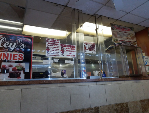 A restaurant counter with glass barriers, menus, and signs displaying service policies and offerings.