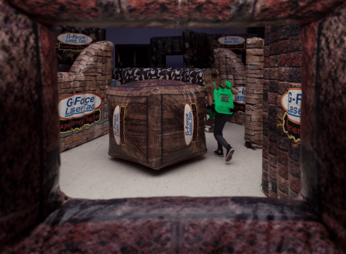 A child in a green hoodie navigates an indoor laser tag arena with inflatable obstacles and themed decorations.