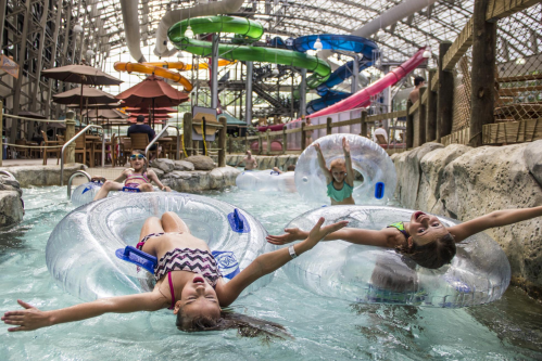 Children enjoying a water park, floating on inner tubes in a lazy river with colorful water slides in the background.