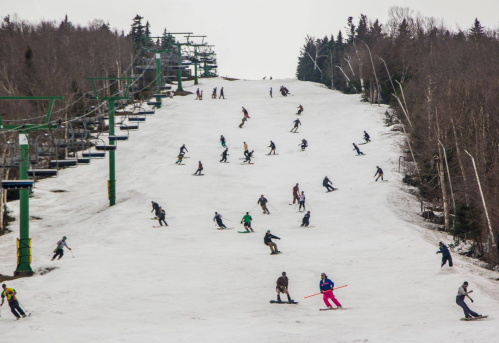 A busy ski slope with numerous skiers and snowboarders enjoying the snow-covered hill. Lifts are visible in the background.
