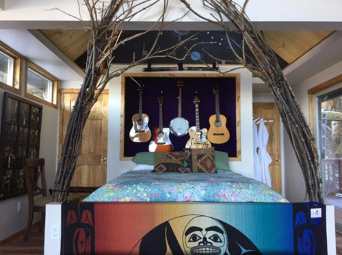 Cozy bedroom featuring a bed with colorful bedding, guitars on the wall, and a unique branch archway.