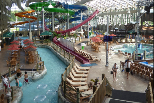 Indoor water park featuring slides, a lazy river, and lounge chairs under umbrellas. Families enjoy the water attractions.