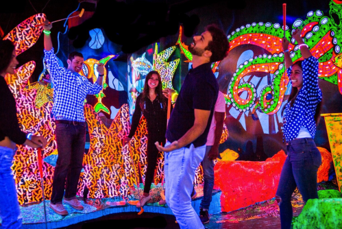 A group of friends enjoying a vibrant, colorful glow-in-the-dark environment with playful poses and smiles.