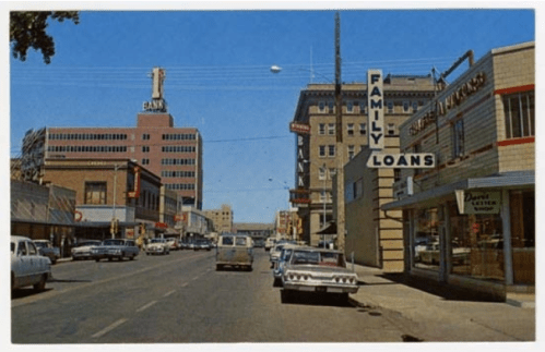A vintage street scene featuring banks and a family loans office, with classic cars parked along the road.