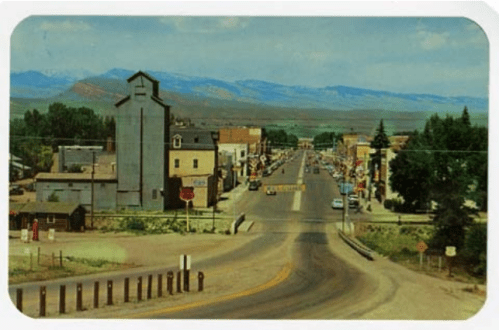 A scenic view of a small town street with mountains in the background and buildings lining the road.