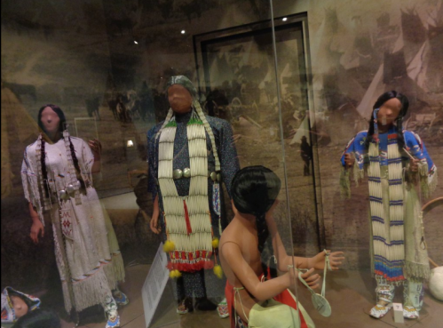 Display of traditional Native American attire in a museum, featuring mannequins dressed in intricate garments and accessories.