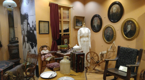 A vintage display featuring a doll, antique furniture, portraits, and historical artifacts in a cozy setting.