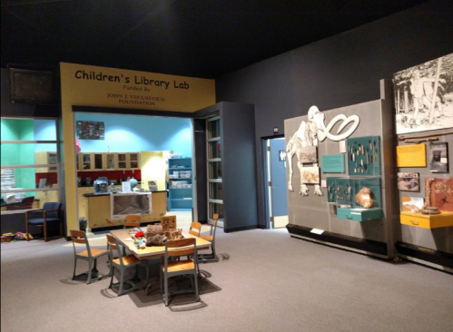 A children's library lab featuring colorful walls, a table with chairs, and educational displays on the walls.
