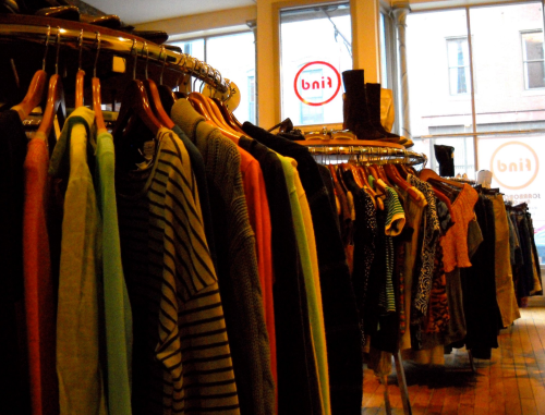 A clothing store interior with racks of colorful garments and a window displaying a sign that reads "bni."
