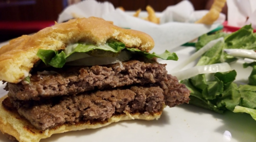 A close-up of a double hamburger with lettuce and onions, served on a plate with a side of fresh greens.