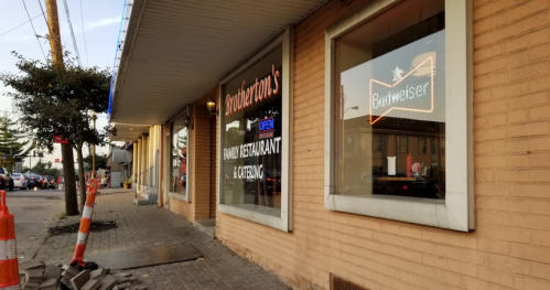 Exterior view of a restaurant with a Budweiser sign, surrounded by construction barriers and a sidewalk.
