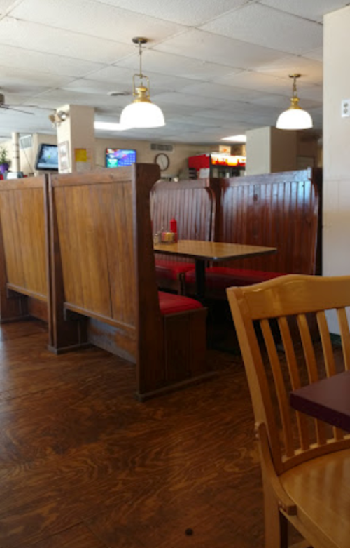 Interior of a casual diner featuring wooden booths, red seating, and overhead lights.