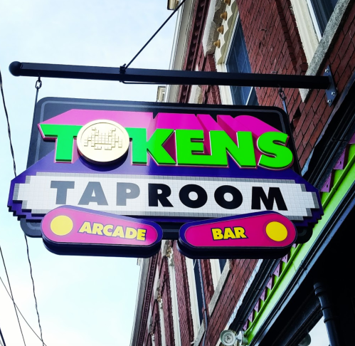 Colorful sign for "Tokens Taproom," featuring arcade elements, indicating it's an arcade bar.