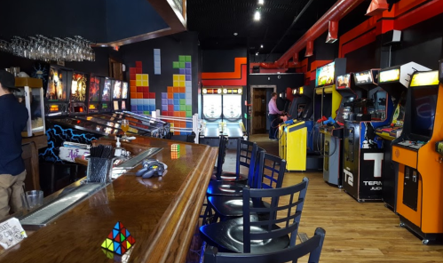 A vibrant arcade with pinball machines, classic arcade games, and a bar area featuring colorful decor and seating.