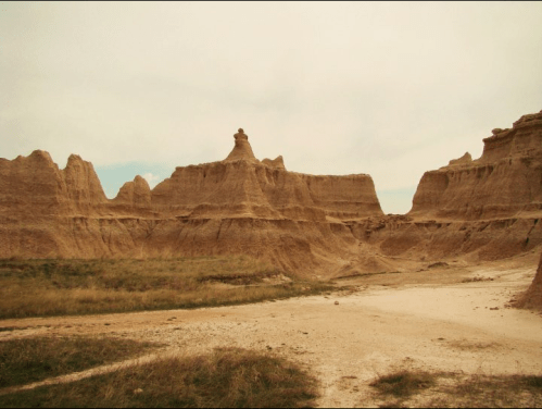 A rugged landscape of eroded rock formations and grassy plains under a cloudy sky.