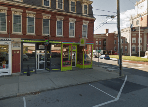 Colorful storefront on a street corner, featuring large windows and a vibrant green entrance, with a brick building behind.