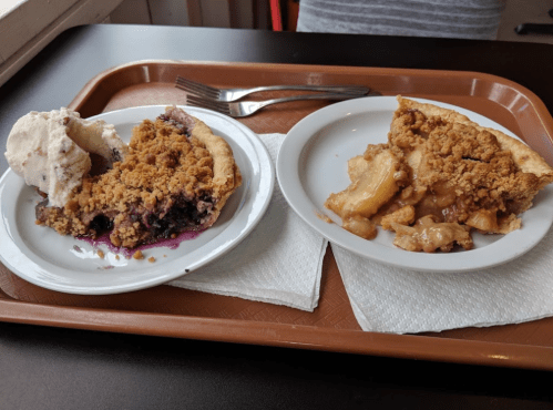 A tray with two slices of pie: one blueberry with ice cream and one apple crumble, both on white plates.