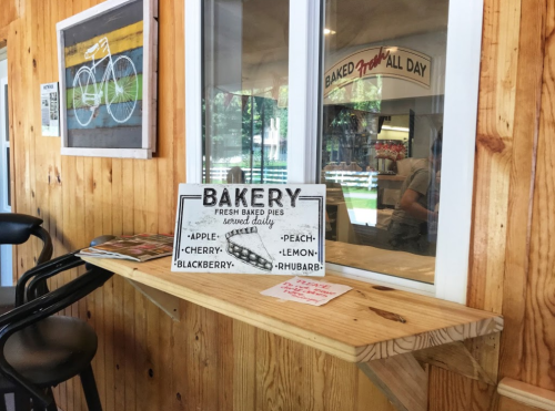 A wooden shelf displays a sign for a bakery offering fresh baked pies, with a cozy interior and bike-themed decor.