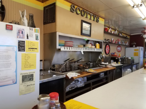 A cozy diner kitchen with a counter, cooking equipment, and colorful plates on display. Walls adorned with memorabilia.