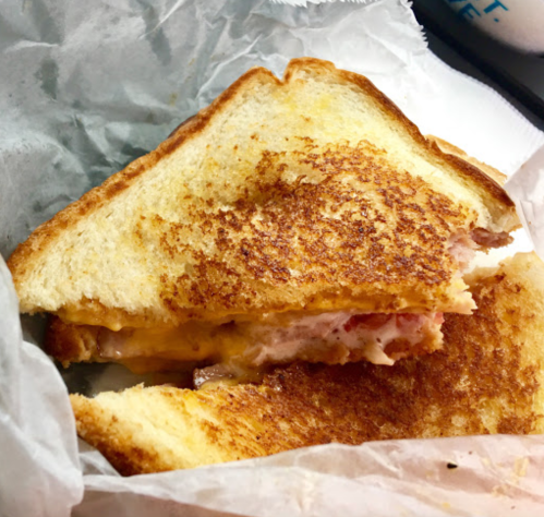 A toasted sandwich with melted cheese and ham, partially cut and wrapped in paper.