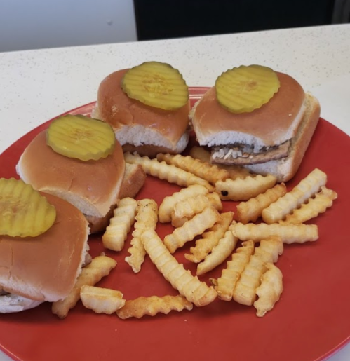 A red plate with three chicken sliders topped with pickles and a side of crinkle-cut fries.