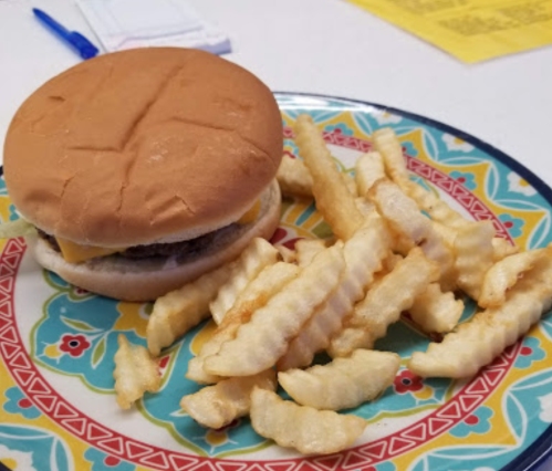 A cheeseburger on a colorful plate with a side of crinkle-cut fries.