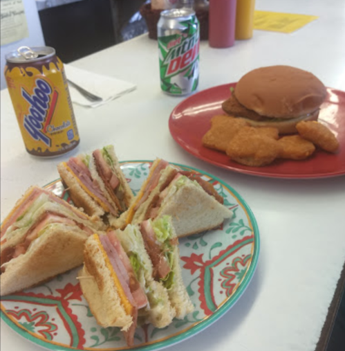 A plate with a sandwich, chicken nuggets, a soda can, and a burger on a red plate.