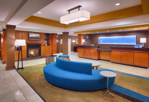 Modern hotel lobby featuring a blue curved sofa, a fireplace, and a reception desk with warm wooden accents.