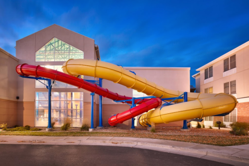 Two large water slides, one red and one yellow, twist outside a building under a twilight sky.