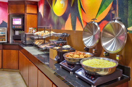 A buffet setup featuring warm dishes, pastries, and a colorful fruit mural in the background.