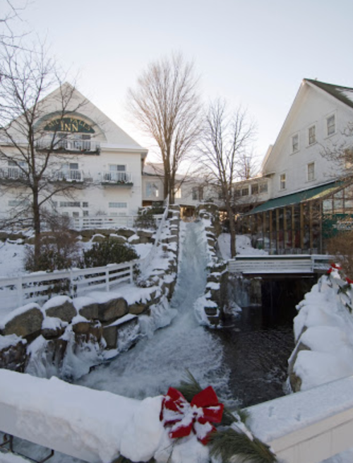 A snowy scene featuring a waterfall, bridge, and a charming inn surrounded by winter trees and decorations.