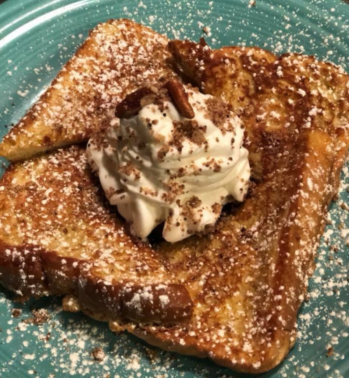 A plate of French toast topped with whipped cream, nuts, and a dusting of powdered sugar on a blue plate.