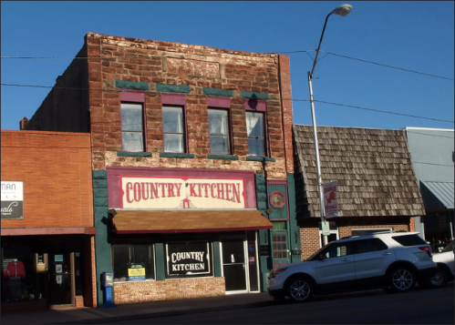 Historic building with a sign reading "Country Kitchen," featuring a rustic facade and nearby parked cars.