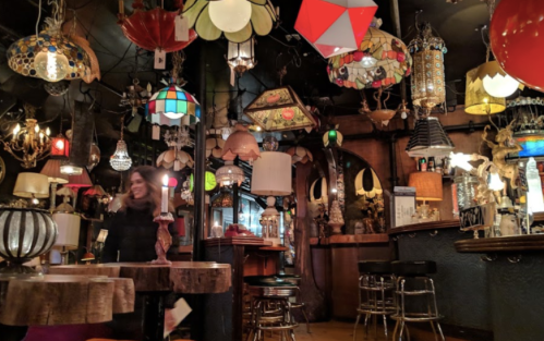 A cozy, eclectic bar filled with various colorful lamps and lighting fixtures, creating a warm atmosphere.