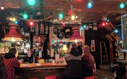 A cozy bar scene with colorful lights, a wooden counter, and patrons enjoying drinks in a warm, inviting atmosphere.
