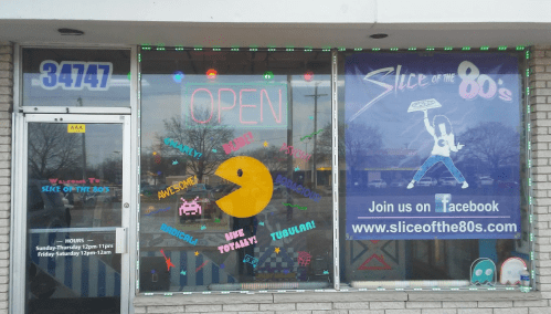 Colorful storefront of "Slice of the 80's" with neon lights, featuring a Pac-Man design and an "Open" sign.
