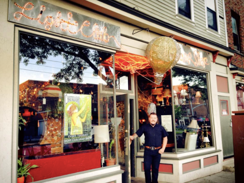 A man stands outside a vibrant light shop with colorful decorations and a large balloon sign.